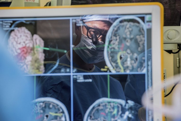 Neurosurgeon Dr. Edward Chang is reflected in a computer monitor displaying brain scans as he performs surgery at the University of California, San Francisco, in 2017. 