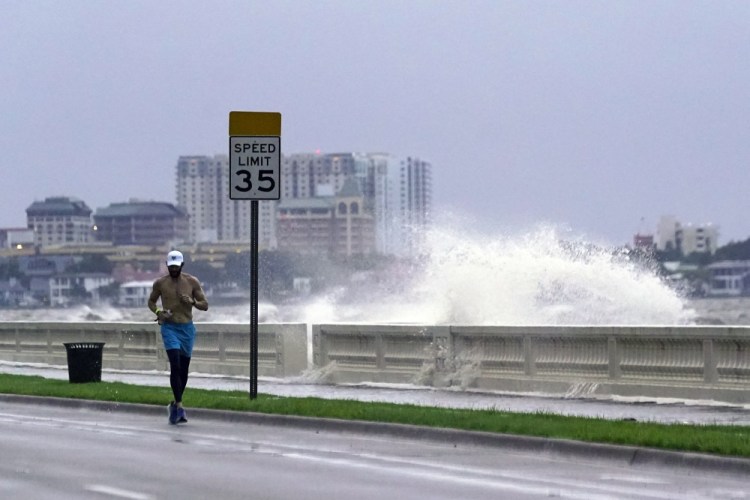 A jogger makes his way along Bayshore Boulevard in Tampa, Fla., as a wave breaks over a seawall, during the aftermath of Tropical Storm Elsa on Wednesday.