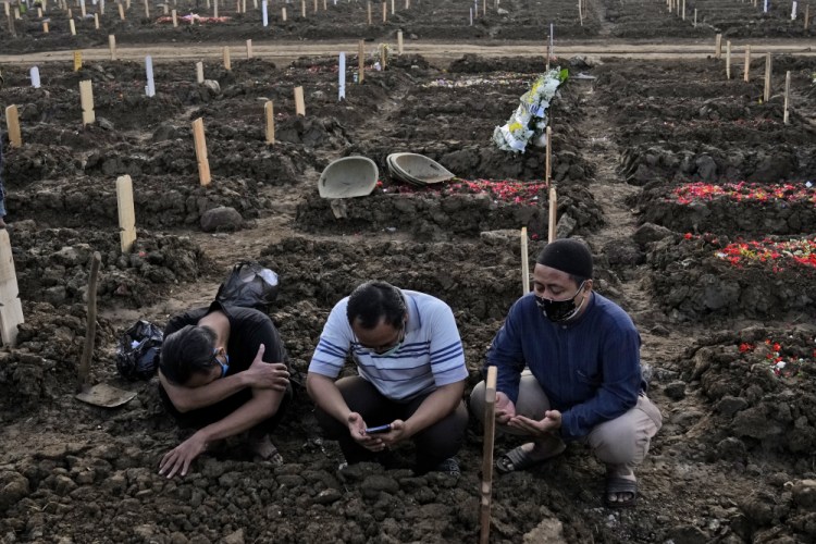 Men pray during the burial of a relative at Rorotan Cemetery, which is reserved for those who died of COVID-19, in Jakarta, Indonesia, on Thursday.
