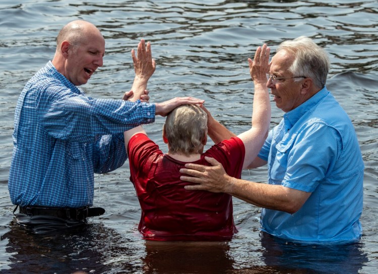 AUGUSTA, ME - AUGUST 21: The Rev. Shane Stoops, left, and The Rev. Rick Stoops, left, pray over a person after they were baptized in the name of Jesus in the waters of the  Kennebec River during an event put on by First United Pentecostal Church of Augusta Saturday August 21, 2021  at the East Side Boat Landing in Augusta. (Staff photo by Joe Phelan/Staff Photographer)