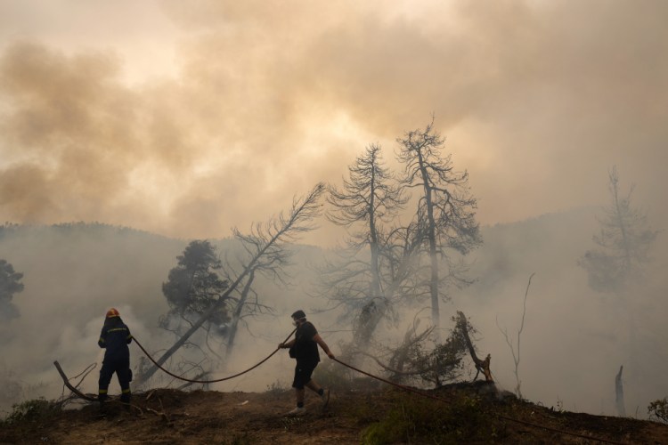 A firefighter tries to extinguish the flames as a local resident holds a hose during a wildfire at Ellinika village on Evia island, about 110 miles north of Athens, Greece, on Monday.


