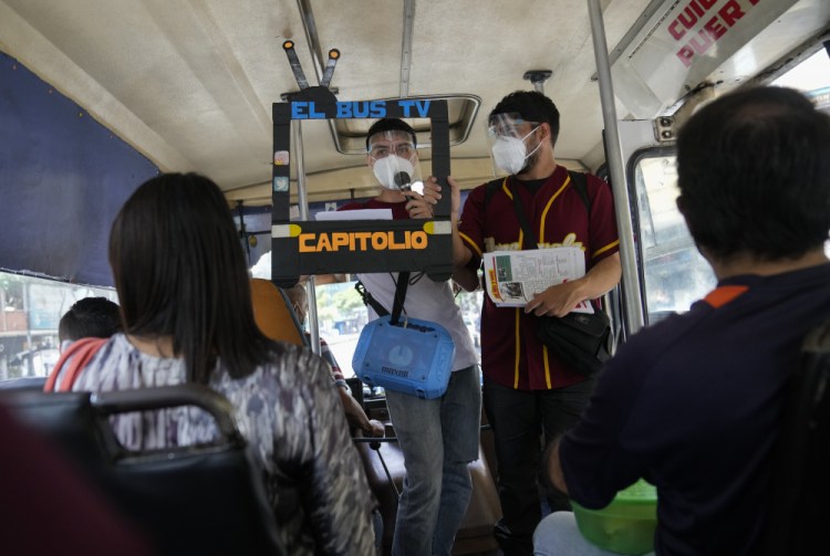 Juan Pablo Lares, right, holds a cardboard frame in front of his associate Maximiliano Bruzual who reads their newscast "El Bus TV Capitolio" to commuters on a bus in Caracas, Venezuela. (AP Photo/Ariana Cubillos)