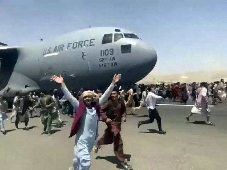 Hundreds of people run alongside a U.S. Air Force C-17 transport plane as it moves down a runway  of the international airport in Kabul, Afghanistan, on Monday. Thousands of Afghans have rushed onto the tarmac of Kabul’s international airport in a desperate attempt to escape the Taliban capture of their country. 