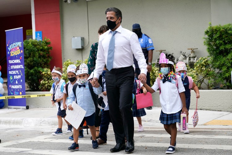 Miami-Dade schools Superintendent Alberto Carvalho, center, walks with students Oliver Angel, left, and Ariah Olawale, right, outside of iPrep Academy on the first day of school, Monday, Aug. 23, 2021, in Miami. Schools in Miami-Dade County opened Monday with a strict mask mandate to guard against coronavirus infections. (AP Photo/Lynne Sladky)