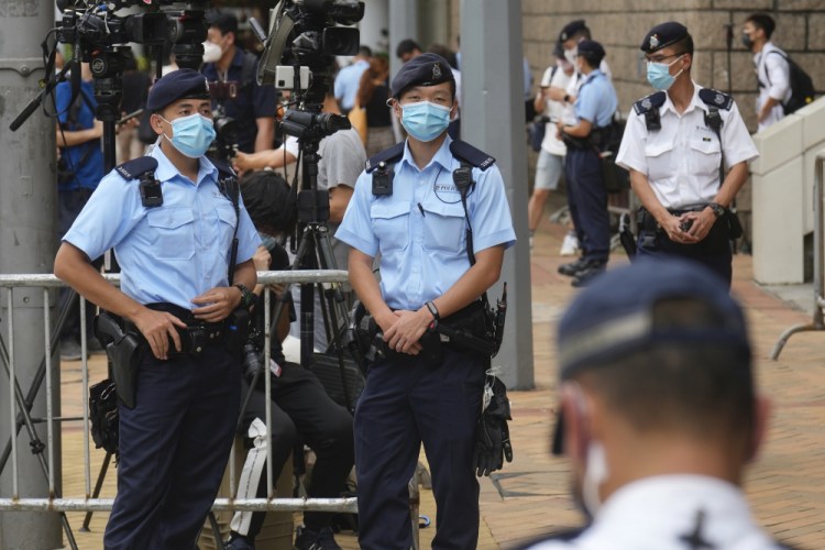 Police officers stand guard outside a court Friday, July 30, 2021, in Hong Kong, as a pro-democracy demonstrator Tong Ying-kit exits the court after his sentencing for the violation of a security law during a 2020 protest. 