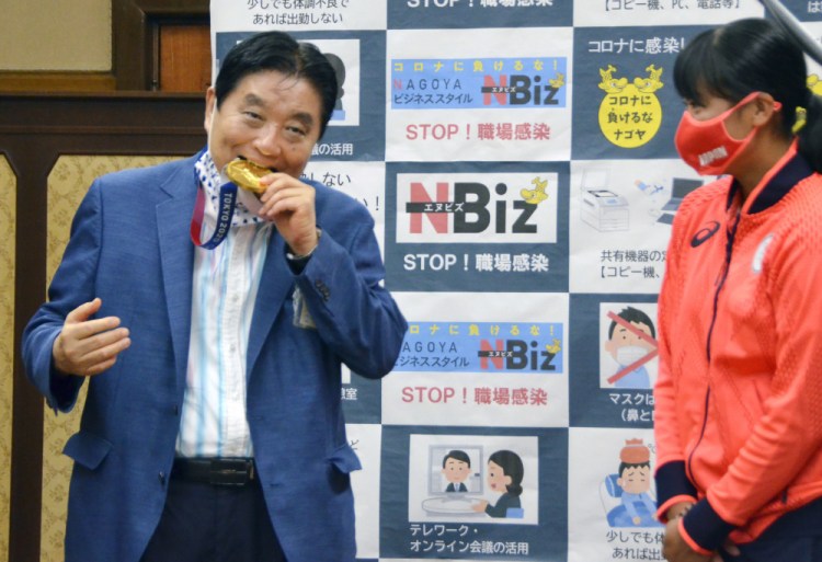 Nagoya Mayor Takashi Kawamura, left, bites the Olympic gold medal of Miu Goto, right, of Japan softball team who won the event at the 2020 Summer Olympics, at the city office building in Nagoya, central Japan, on Wednesday. 