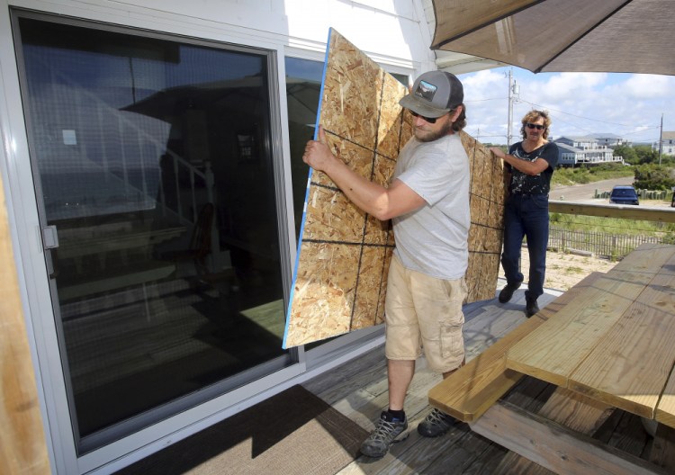 James Masog, center, and Gary Tavares, right, move particle board into place Saturday to protect the sliding glass doors of a client's house in Charlestown, R.I.
