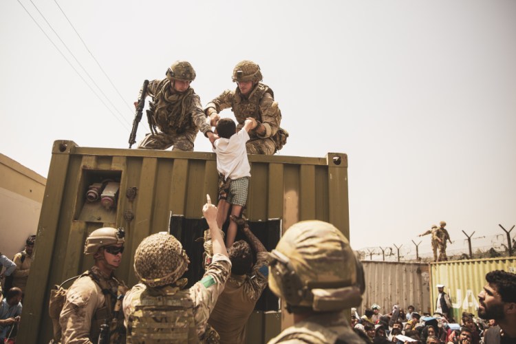 In this image provided by the U.S. Marine Corps, British and Turkish coalition forces, along with U.S. Marines, assist a child during an evacuation at Hamid Karzai International Airport in Kabul, Afghanistan, on Friday.