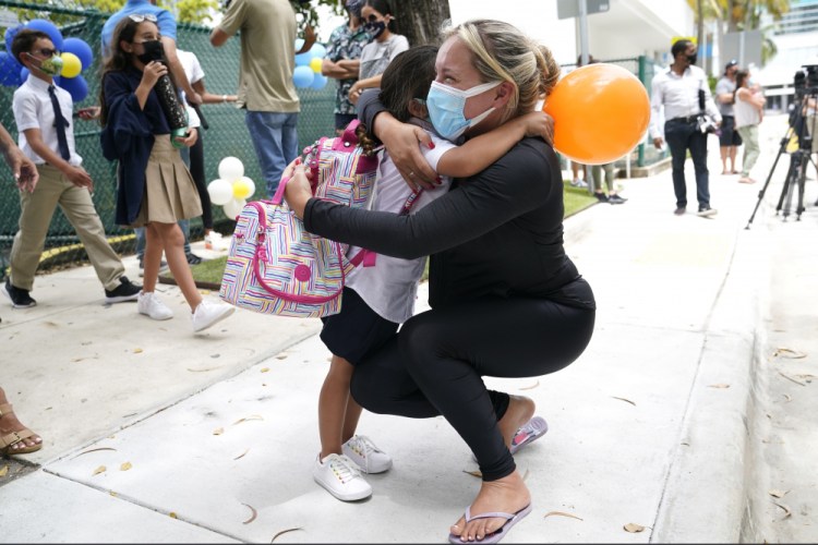Carol Basilio, right, hugs her daughter Giovanna outside of iPrep Academy on Aug. 23, the first day of school, in Miami. A judge has ruled that Florida school districts may impose mask mandates. Leon County Circuit Judge John C. Cooper on Friday agreed with a group of parents who claimed in a lawsuit that Gov. Ron DeSantis' ban on the mandates is unconstitutional and cannot be enforced. 