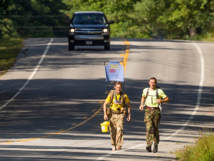 Chris Brannigan, left, joined by Stuart Aitken of Cumberland, makes a barefoot march along Route 201 between Gardner and Brunswick on Monday, part of a 1,200-mile trek to raise awareness and funds for his daughter's fight against a rare disease.