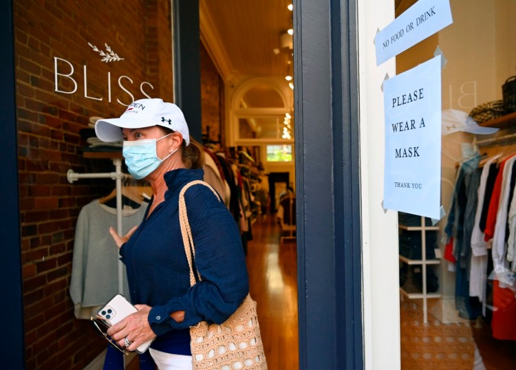 Maureen Dodson of Brigantine, N.J., leaves Bliss in the Old Port, where a sign encourages visitors to wear masks Monday. On Monday night, the Portland City Council considered making masks mandatory in public indoor spaces but delayed its vote.
