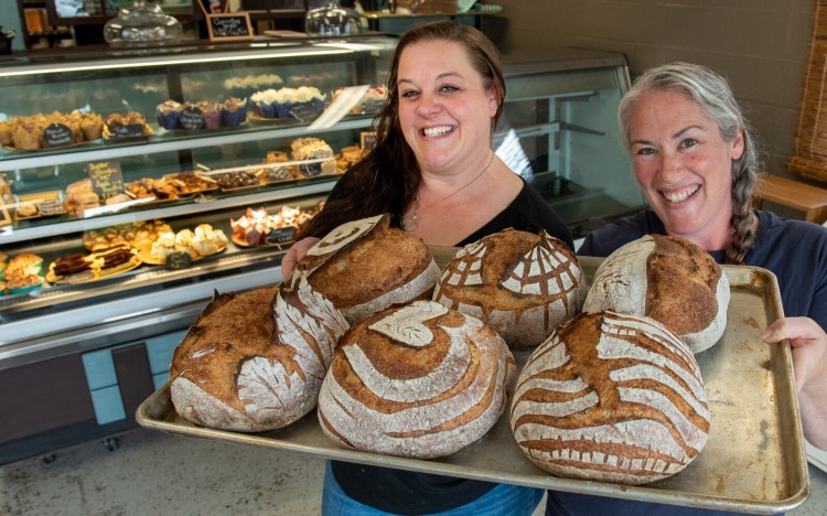 Sarah Farrell, left, and Meaghan Braun, co-owners of Bakery Barn on Lisbon Street in Lewiston, show a tray of their artisan sourdough bread Wednesday morning with a well-stocked cooler of sweet treats in the background. Braun's boyfriend, Eric Goode, baked the bread using locally sourced organic grains.