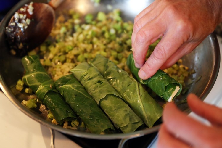 Placing the feta-stuffed rolled collards into the pan to cook.