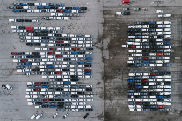 Mid-sized pickup trucks and full-size vans are seen in a parking lot outside a General Motors assembly plant where they are produced in Wentzville, Mo. in March. The global shortage of computer chips is getting worse, forcing automakers to temporarily close factories including those that build popular pickup trucks. 