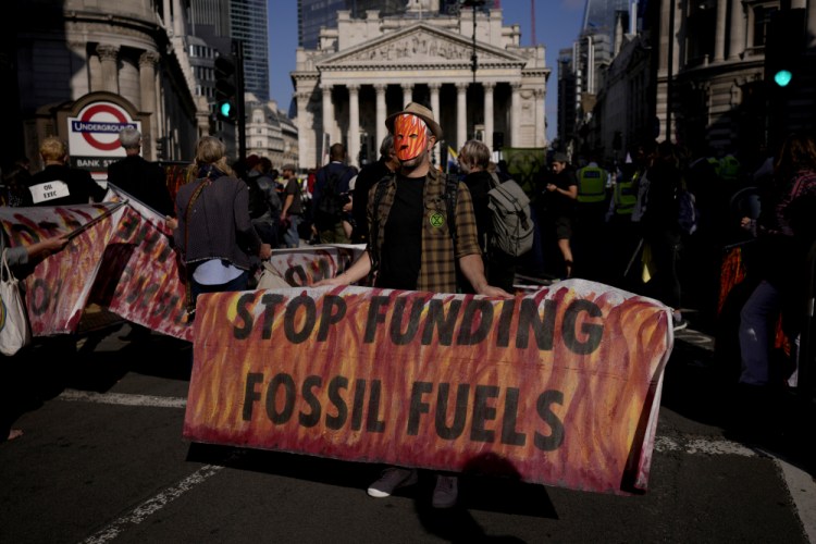 An Extinction Rebellion climate change activist holds a banner backdropped by the Bank of England, at left, and the Royal Exchange, center, in the City of London financial district in London on Sept. 2, 2021. 