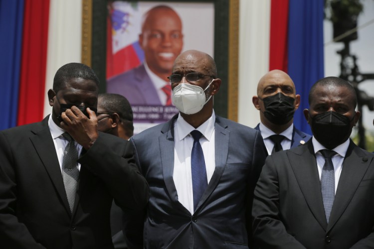 Haiti's designated Prime Minister Ariel Henry, center, and interim Prime Minister Claude Joseph, right, pose for a group photo with other authorities in front of a portrait of slain Haitian President Jovenel Moise at the National Pantheon Museum during a memorial service for Moise in Port-au-Prince, Haiti, in July. Haiti’s chief prosecutor has asked a judge to charge Henry in the slaying of Moise and barred him from leaving the country. 