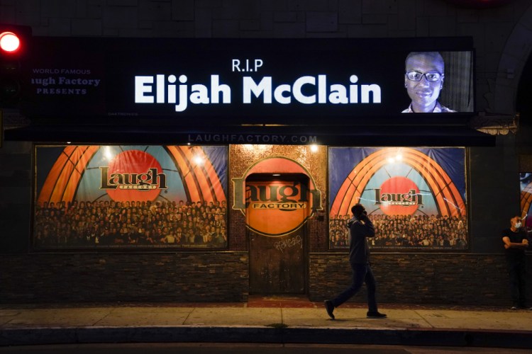 A man walks past a display showing an image of Elijah McClain outside Laugh Factory during a candlelight vigil for McClain in Los Angeles in August 2020.   Colorado’s attorney general said Wednesday that a grand jury indicted three officers and two paramedics in the death of McClain, a Black man who was put in a chokehold and injected with a powerful sedative two years ago in suburban Denver. 