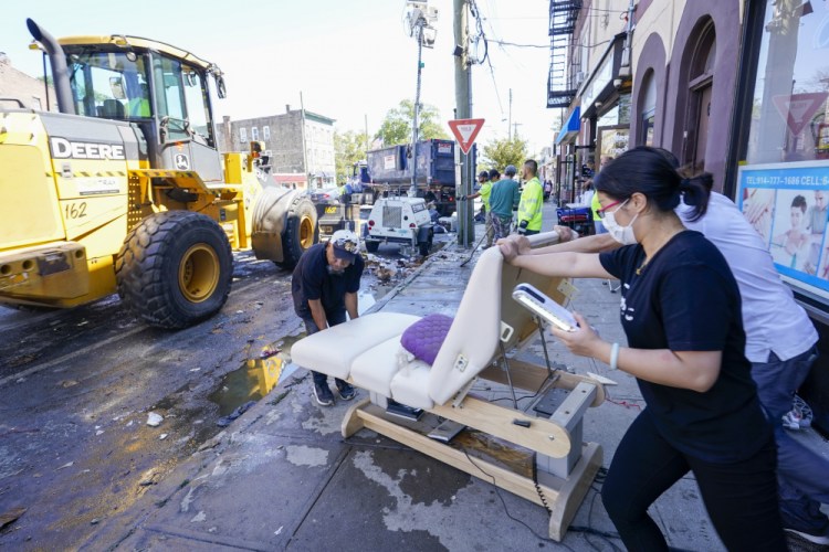 Business owner put out water logged equipment as Village of Mamaroneck workers use a front loader to remove water logged items from the sidewalk after remnants of Hurricane Ida inundated the community, Saturday in Mamaroneck, N.Y. 