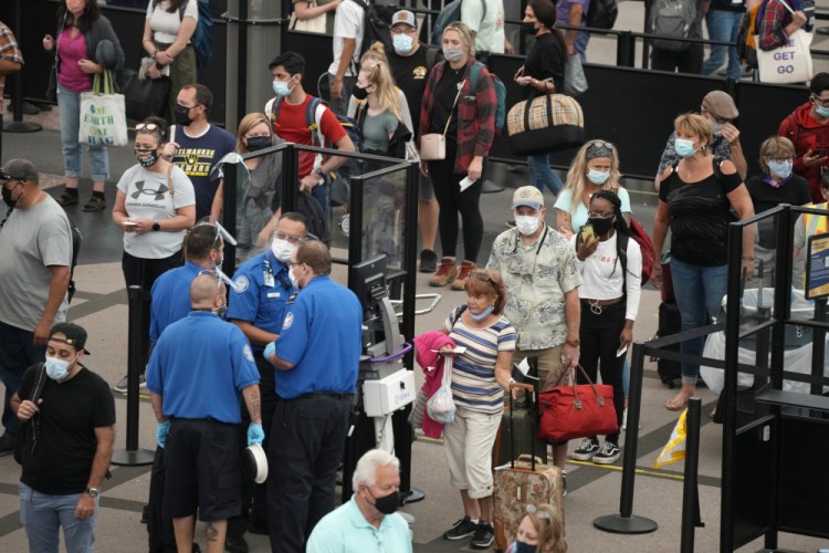 Travelers wear face coverings while waiting in line for a security checkpoint in the main terminal of Denver International Airport in August in Denver. 