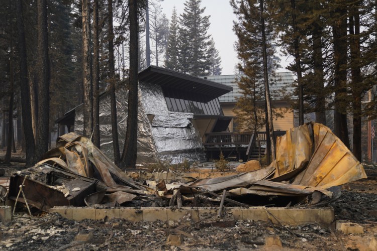 FILE - In this Sept. 2, 2021 file photo a cabin partially covered in fire-resistant material stands behind a property destroyed in the Caldor Fire in Twin Bridges, Calif.  Aluminum wraps designed to protect homes from flames are getting attention as wildfires burn in California. During a fire near Lake Tahoe, some wrapped houses survived while nearby homes were destroyed. The material resembles tin foil from the kitchen drawer but is modeled after the tent-like shelters that wildland firefighters use as a last resort to protect themselves when trapped by flames.  (AP Photo/Jae C. Hong,File)