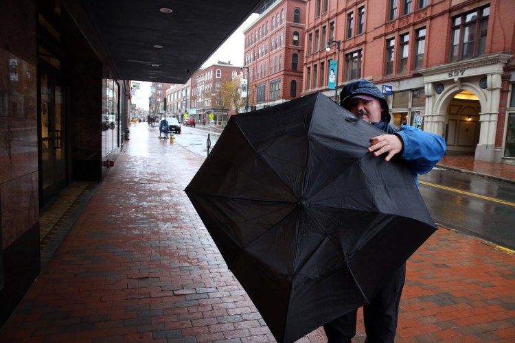 Arthur Moore of Portland attempts to bend his umbrella back into shape after the wind on Tuesday turned it inside-out on Congress Street in Portland. 