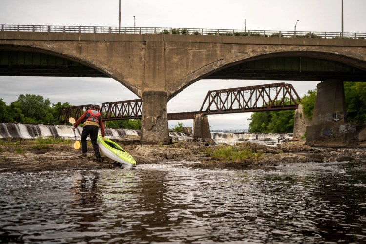 Hunter Smith hauls his kayak onto an outcrop of rocks in June as he looks for a spot to fish for striped bass under the Ticonic Bridge on the Kennebec River between Waterville and Winslow. The bridge is poised to undergo a $40.5 million overhaul and leaders in the two cities are lobbying state transportation officials to close the bridge entirely during construction rather than keeping a lane open for traffic. Such a move would speed up the construction timeline.