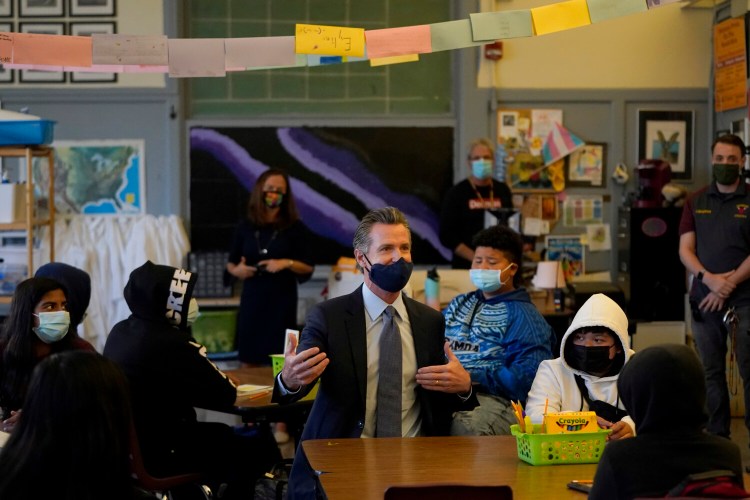Gov. Gavin Newsom, middle, speaks to students in a seventh grade science class at James Denman Middle School in San Francisco, Friday, Oct. 1, 2021.  California has announced the nation's first coronavirus vaccine mandate for schoolchildren.   Newsom said Friday that the mandate won't take effect until the COVID-19 vaccine has received final approval from the U.S. government for various grade levels. (AP Photo/Jeff Chiu)