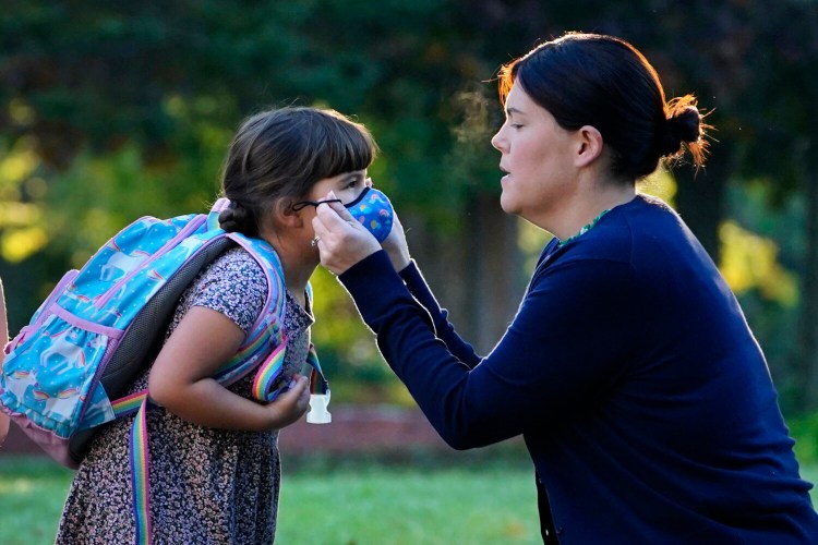 Sarah Staffiere adjusts a face covering on her daughter Natalie before school recently in Waterville. Staffiere, a senior laboratory instructor at Colby College, said she will be relieved when her two children can be vaccinated. 