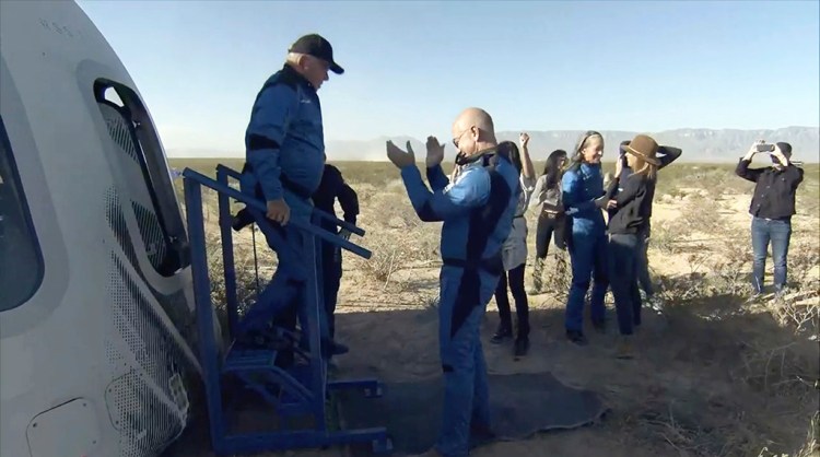 In this image provided by Blue Origin, William Shatner exits the Blue Origin capsule as he is greeted by Jeff Bezos near Van Horn, Texas, Wednesday, Oct. 13, 2021.  The “Star Trek” actor and three fellow passengers hurtled to an altitude of 66.5 miles (107 kilometers) over the West Texas desert in the fully automated capsule, then safely parachuted back to Earth in a flight that lasted just over 10 minutes.  (Blue Origin via AP)