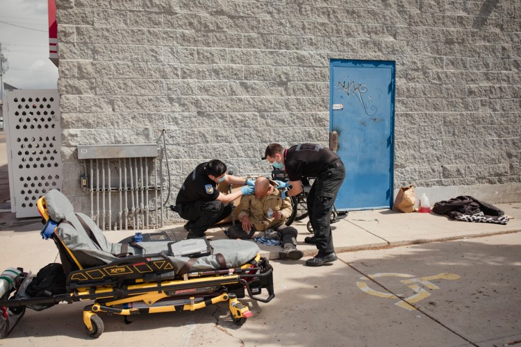 Emergency medical personnel, called by behavioral health responders, assist an unsheltered man who had collapsed outside a vacant gas station in Albuquerque, N.M. MUST CREDIT: photo for The Washington Post by Adria Malcolm.