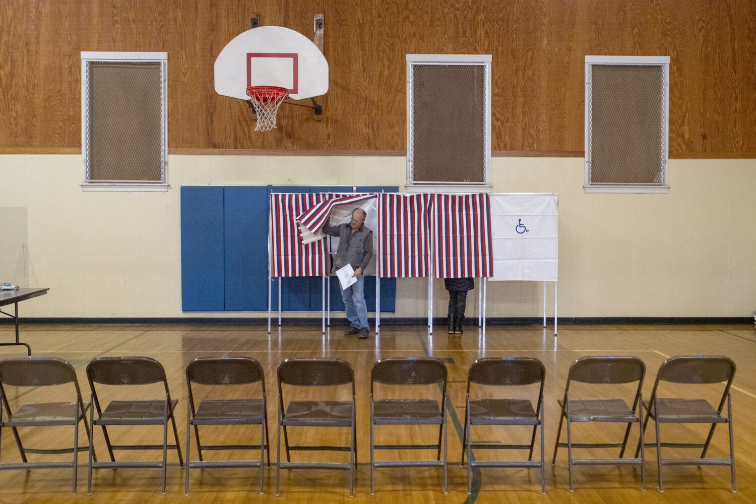 Man emerging from voting booth in otherwise empty gym
