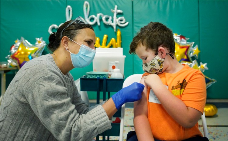 Finley Wetzel, a kindergartner at Pond Cove School in Cape Elizabeth, watches as Dr. Karen Emery applies a bandage after administering a Pfizer vaccine during a clinic at the school in November. Emery is a pediatrician with Maine Medical Partners Falmouth Pediatrics. 