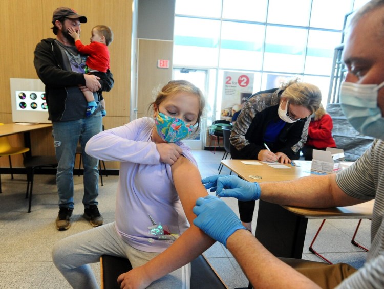 Accompanied by members of her family, 9-year-old Lily Taylor of Skowhegan yanks up her sleeve as Oakland Pharmacy’s Shane Savage prepares to administer her COVID-19 vaccination at a pop-up clinic at the McDonald’s in Waterville last week.