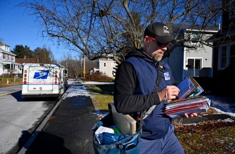 John Graham sorts through mail while making deliveries on Ray Street in Portland in Dec. 2021. While he once expected to deliver 10 to 20 packages a day, he says it's now more like 120 a day, and more during the holidays.