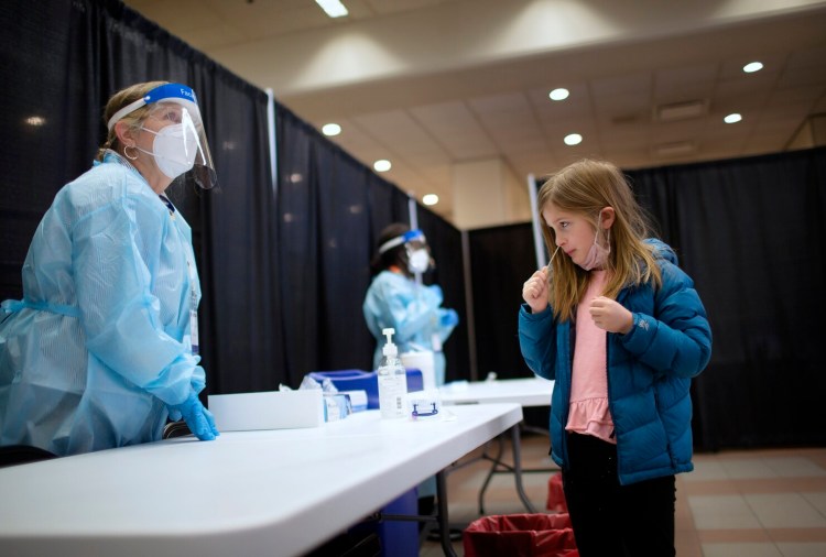 Sadie Wieland of Scarborough swabs her nose while Ann Marie Ray, site lead, talks to Sadie's mother on Dec. 15 at the Portland International Jetport, where COVID testing was administered by Curative. 