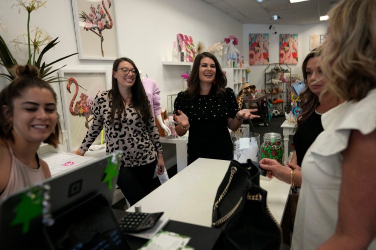Prep Obsessed business co-owners Corey O'Loughlin, center, and Nina Vitalino, center left, laugh as they talk with customers checking-out in their retail store in Palm Beach Gardens, Fla., Thursday, Dec. 16, 2021. O’Loughlin and Vitalino co-own Prep Obsessed, an online boutique that also has a brick-and-mortar location. Black Friday sales jumped more than 30% over last year, a relief for the owners. (AP Photo/Rebecca Blackwell)
