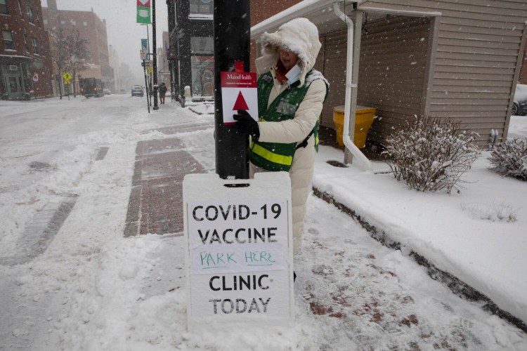 Andrea Gerstenberger, a MaineHealth employee, posts directions on Free Street for a COVID-19 vaccine clinic during Friday’s snowstorm in Portland. Research has shown that fully vaccinated and boosted individuals are not getting as sick, even from the omicron variant.