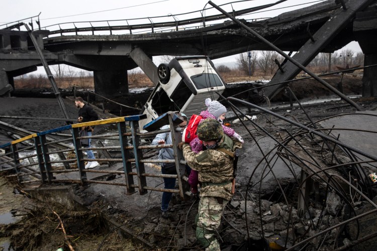A Ukrainian commander carries a young girl as he helps people flee across a destroyed bridge on the outskirts of Kyiv, Ukraine, on Thursday. Ukrainian forces say Russian fighters destroyed the bridge. MUST CREDIT: Photo for The Washington Post by Heidi Levine