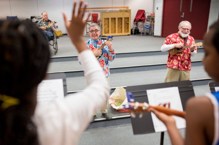 Lee Urban, at left, answers a question from one of his students during a ukulele camp at Riverton Elementary School in 2018. The camp is run by Urban, founder of the nonprofit Ukuleles Heal the World. Fellow ukulele players and teachers, like Duncan Perry, at right, also volunteer to help teach the kids.