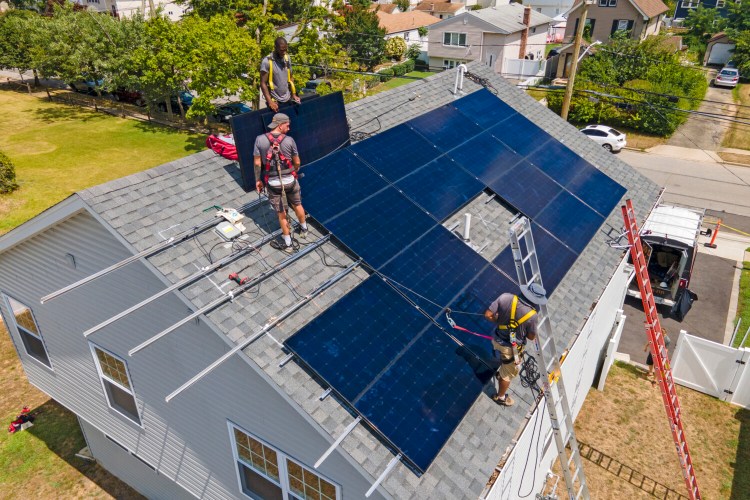 Workers with NY State Solar, a solar panel sales and installation company, install 415 DC watt solar panels onto the roof of a home in Massapequa, New York, on Thursday. The Inflation Reduction Act expands a tax credit for homeowners who invest in energy-efficient equipment, from a one-time $500 credit to $1,200 that homeowners could claim annually. 