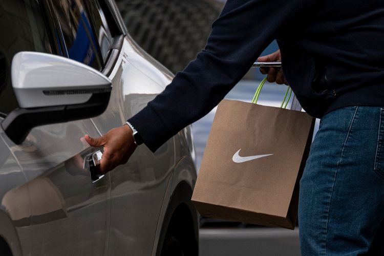 A person wearing a protective mask carries a Nike branded shopping bag in front of a Nike store in San Francisco, California, U.S., on Monday, March 15, 2021.