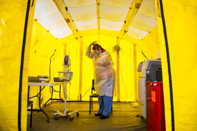 Nurse practitioner Amy Israelian puts on protective gear in a tent in the parking lot of a hospital before testing a patient in Newton, Mass., on March 16, 2020. 